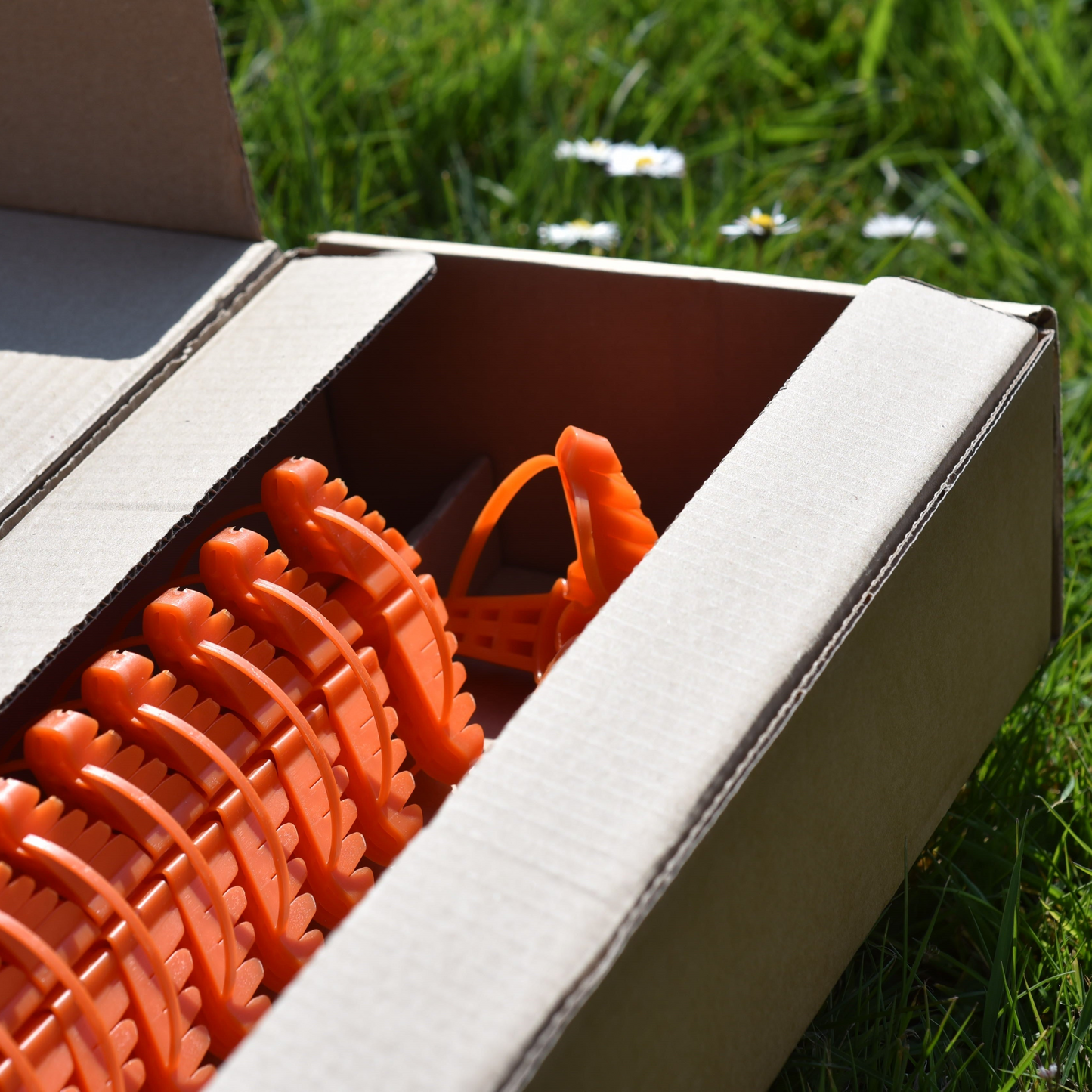 Open cardboard box with orange plant support tools on a grassy background