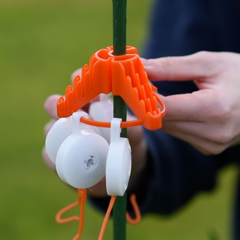 Orange plant support tool being used on a green stem with a blurred background